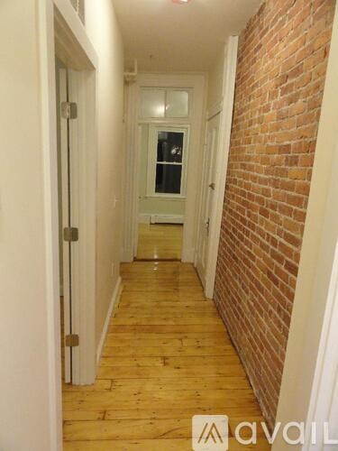 A hallway with a wooden floor and a brick wall.