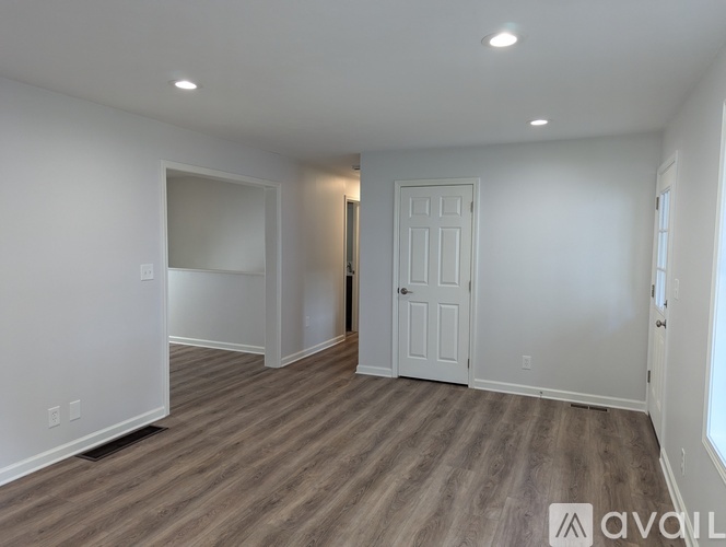 A room with wooden flooring and white walls, with a door and a window.