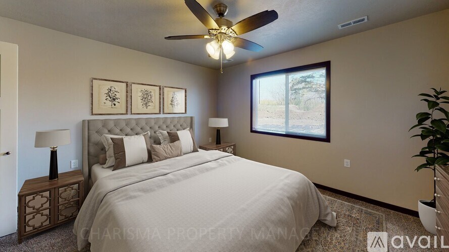 A bedroom with a large bed, a ceiling fan, and a window with a view of trees outside.