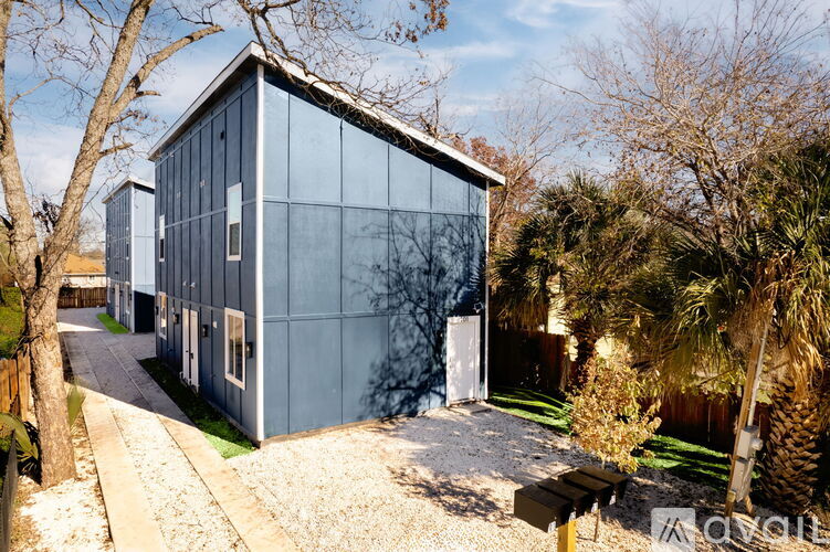 A modern house with a glass facade is surrounded by trees and a gravel path.