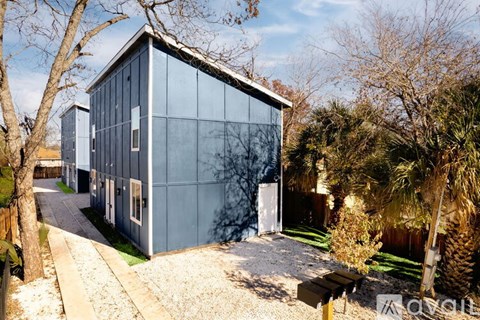 A modern house with a glass facade is surrounded by trees and a gravel path.