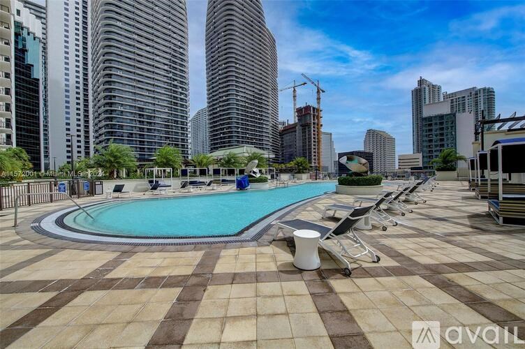 A large outdoor pool area with a tiled floor and a blue pool surrounded by lounge chairs and umbrellas.