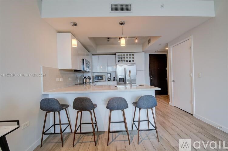 A kitchen with white cabinets and a bar area with grey stools.