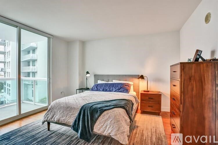 A bedroom with a bed, nightstand, and a balcony with a view of a building.