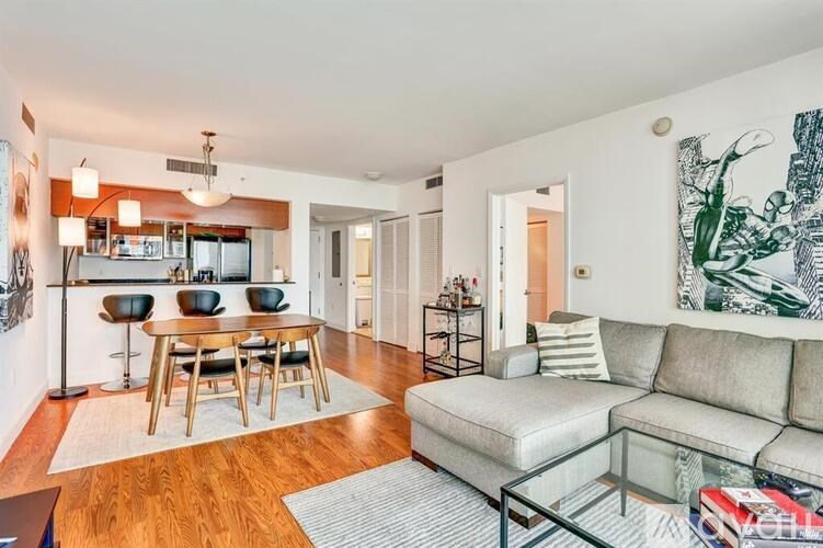 A living room with a couch, a dining table, and a kitchen area in the background.