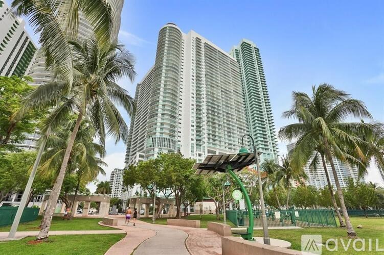 A park with palm trees and a walkway leading to a tall building.