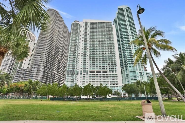 A tall building with a glass facade stands in front of a row of palm trees.