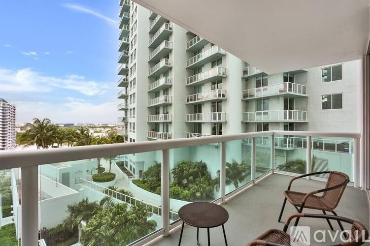 A balcony with a table and chairs overlooks a courtyard and apartment building.