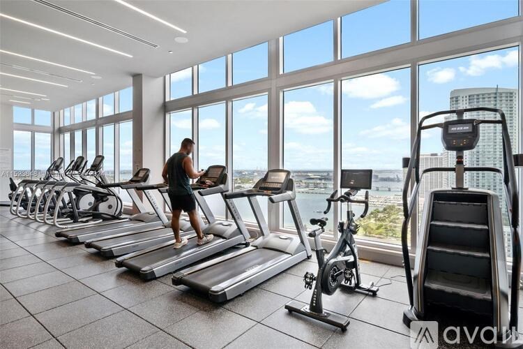 A man is running on a treadmill in a gym with a view of the city.