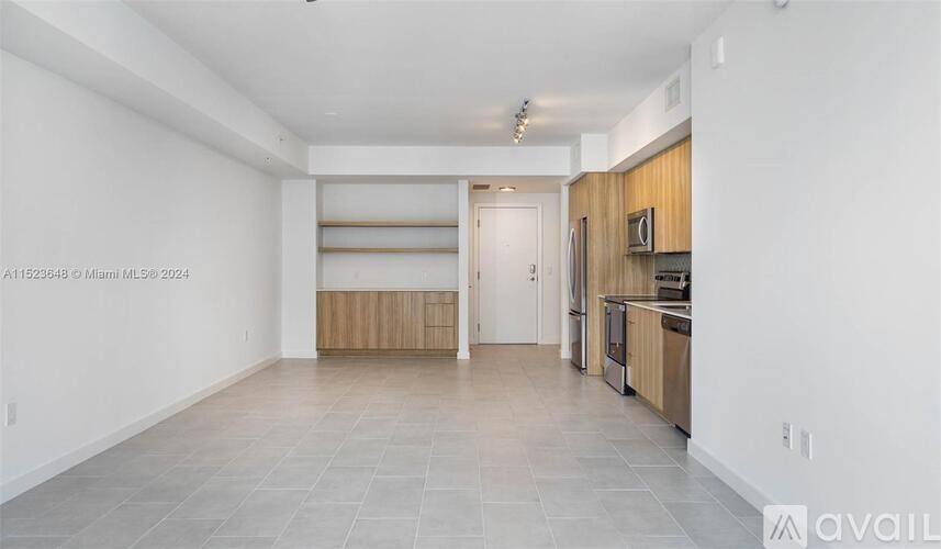 A spacious, empty room with a kitchen area in the background.