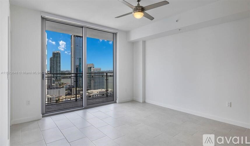 A room with a ceiling fan and sliding glass doors that open to a city view.