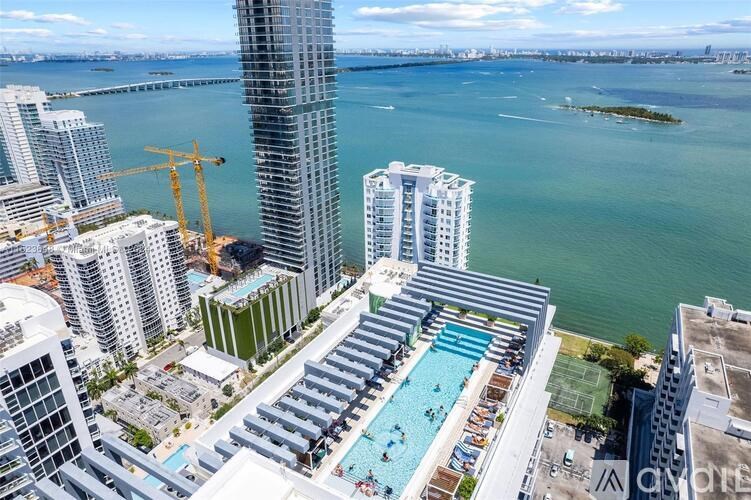 A view of a city with a pool in the foreground and a body of water in the background.