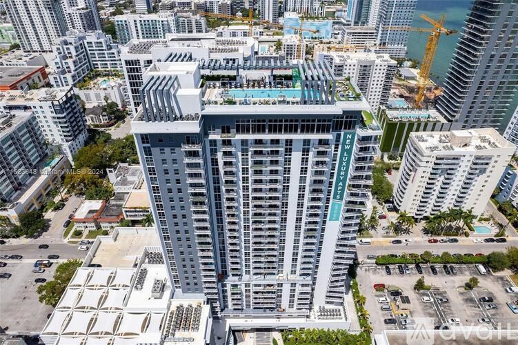 A tall building with a pool on the top floor is surrounded by other buildings.