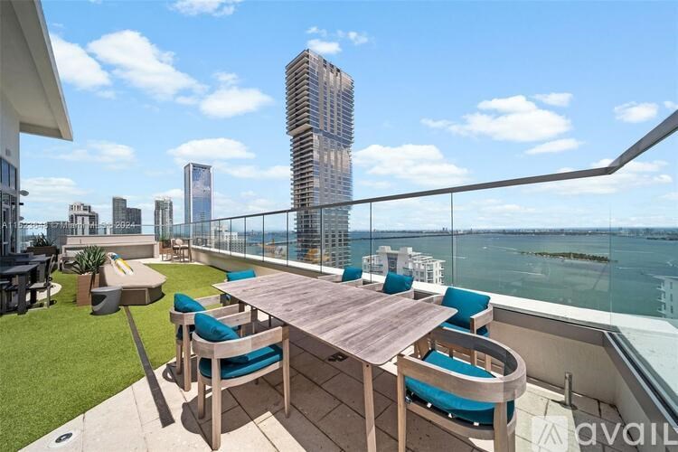 A wooden table with blue chairs is on a balcony overlooking the water.