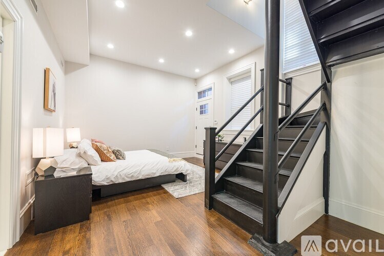 A bedroom with a bed, nightstand, and staircase.