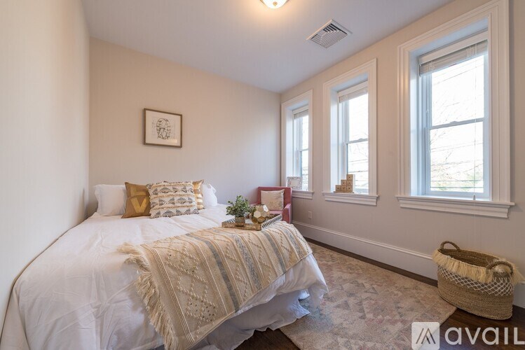 A bedroom with a bed, pillows, a basket, and a framed picture on the wall.