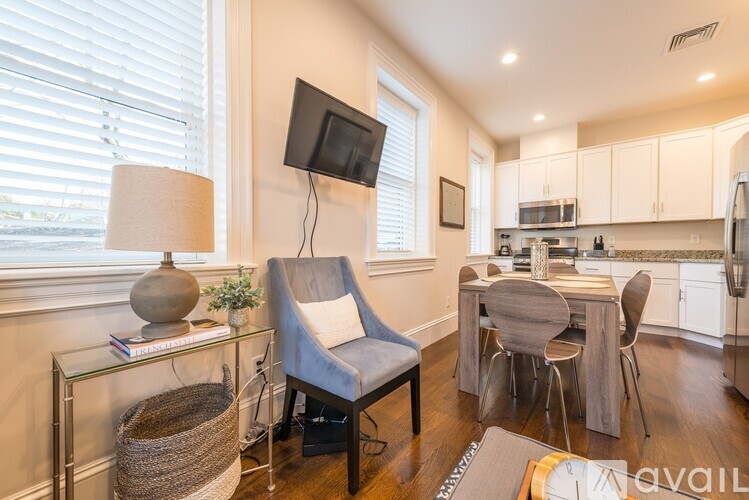 A living room with a grey chair and a glass table with a lamp and a plant on it.