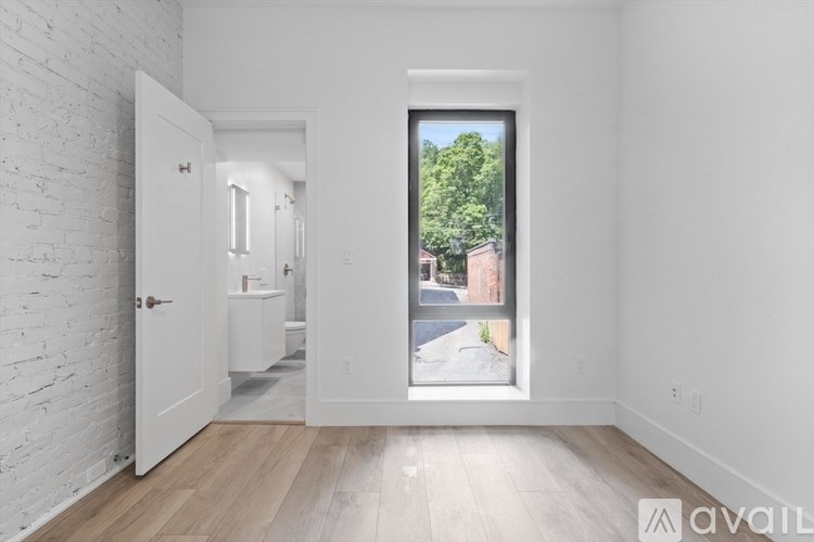 A white interior with a doorway leading to a bathroom and a window showing an outdoor view.