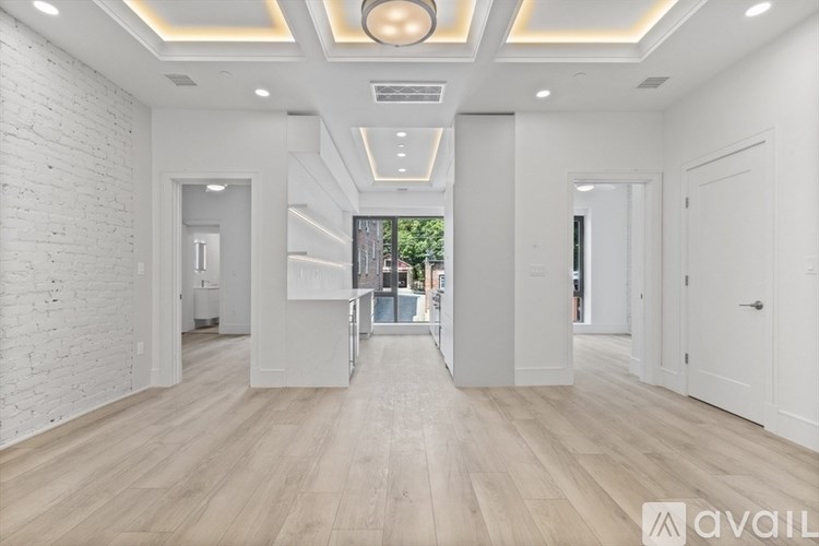 A spacious room with wooden floors and white walls, with a view of greenery outside the window.