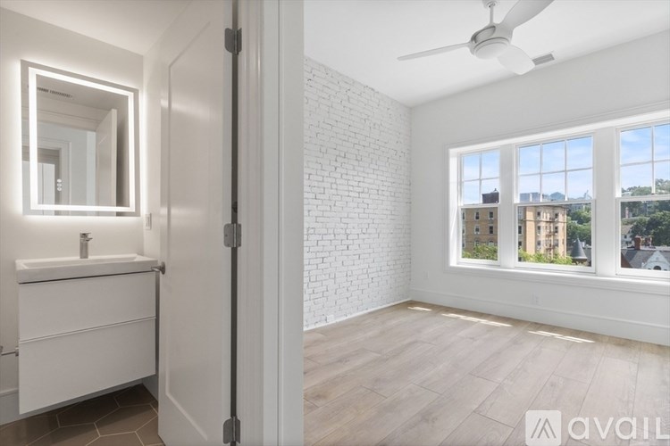 A bathroom with a white sink and mirror, wooden flooring, and a window with a view of buildings outside.