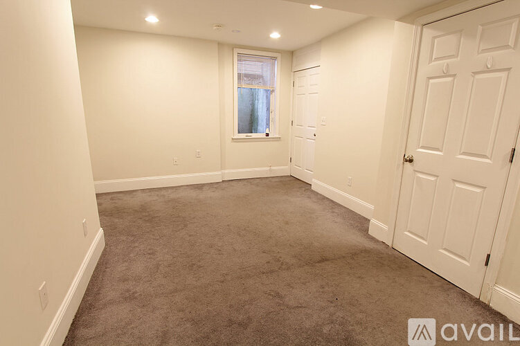 A room with a carpeted floor and a window with a view of a building outside.