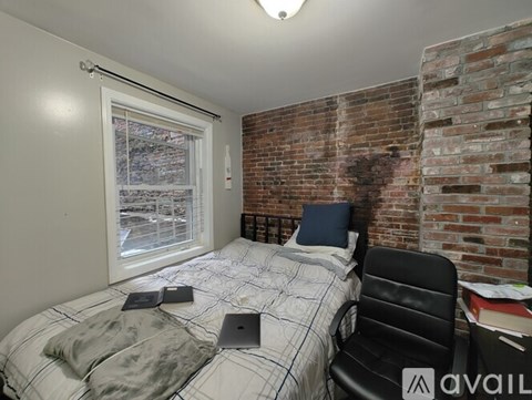 A bedroom with a brick wall and a bed with a laptop on it.