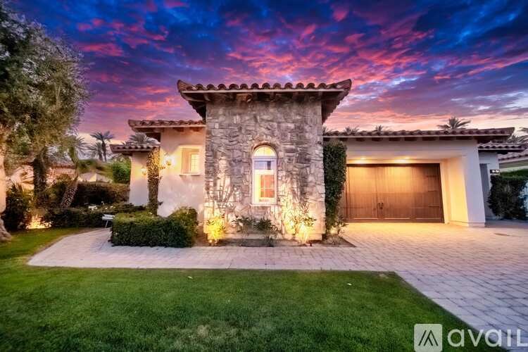 A house with a stone tower and a garage is illuminated by lights.