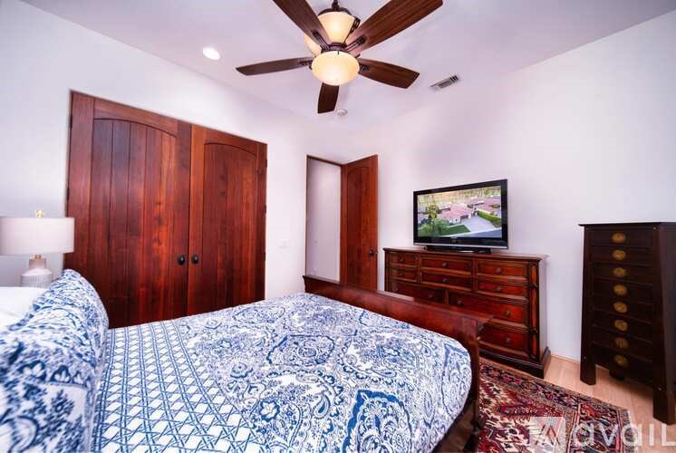 A bedroom with a patterned bedspread and a ceiling fan.