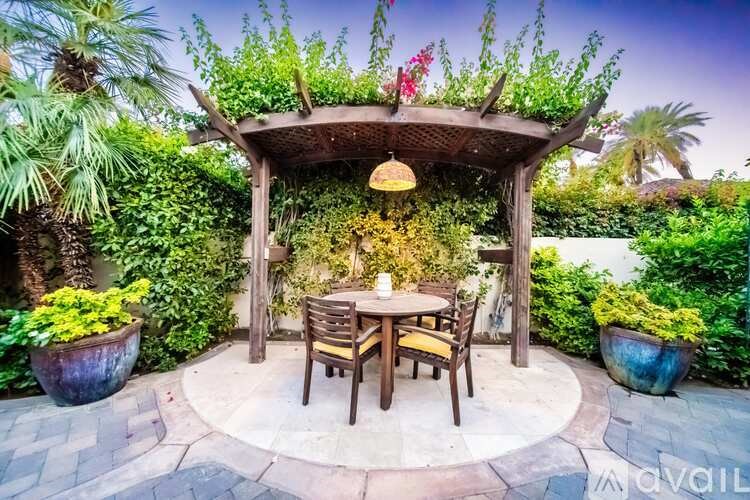 A wooden table and chairs are set up under a wooden pergola with a hanging light.