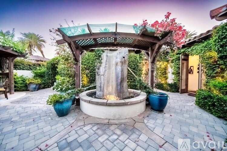 A gazebo with a waterfall in the middle of a garden.