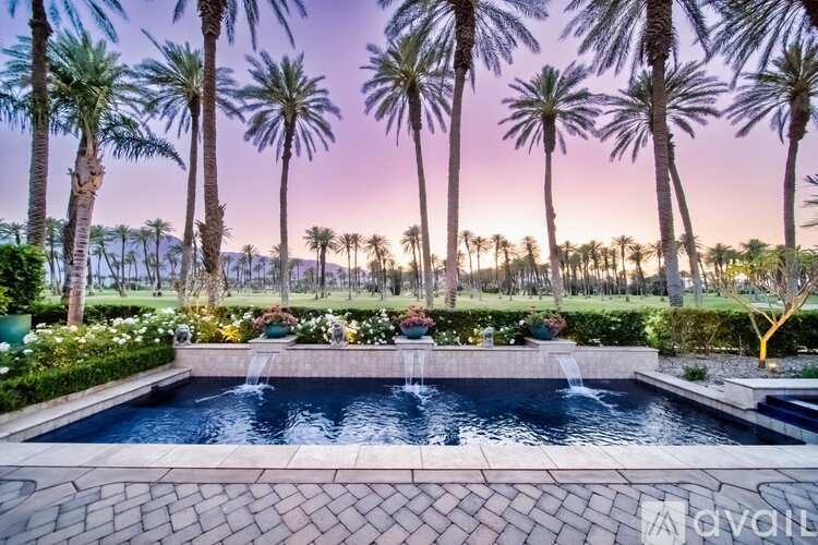 A pool surrounded by palm trees and flowers at dusk.