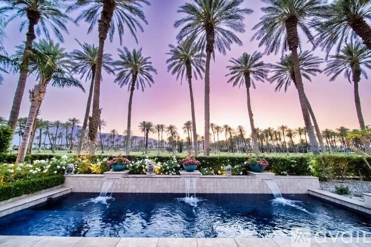 A pool surrounded by palm trees and flowers at dusk.