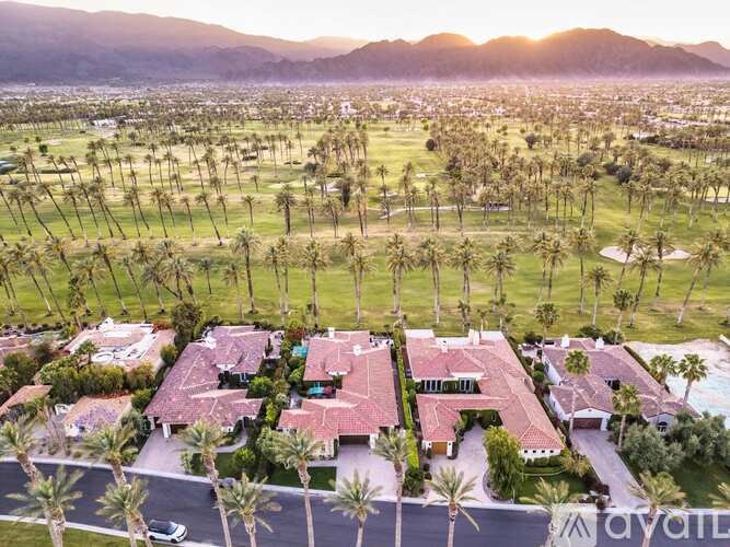 A large house with a red roof is surrounded by palm trees.