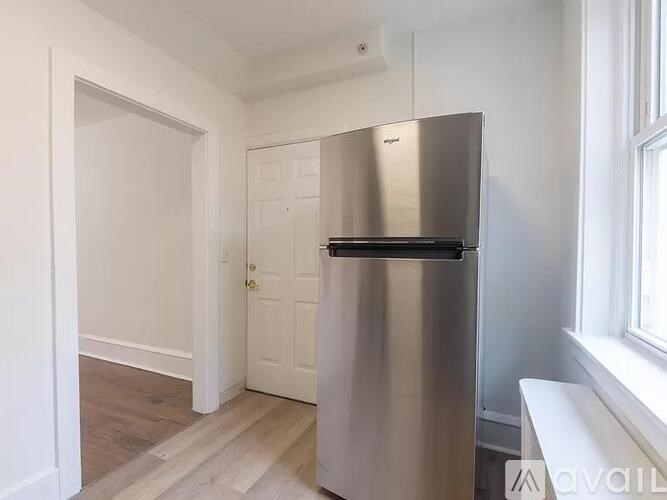 A stainless steel refrigerator in a kitchen with white walls and wooden flooring.