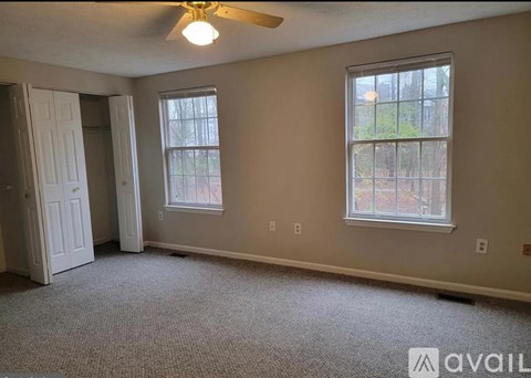 A room with a carpeted floor, a ceiling fan, and two windows.