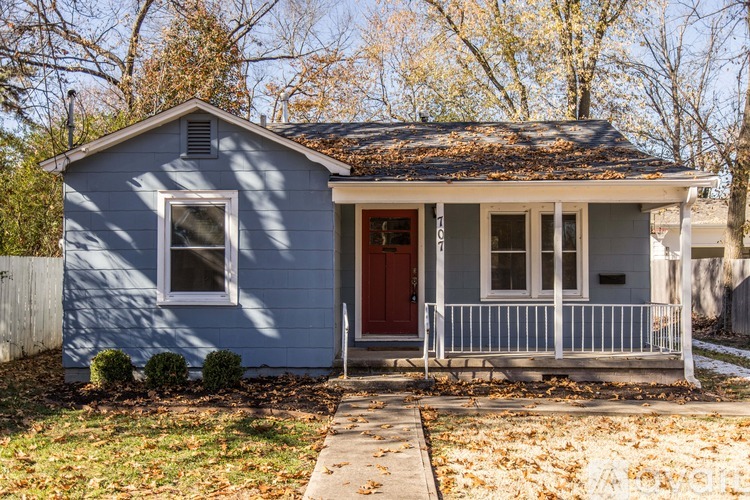 A small blue house with a red door and a grey porch.