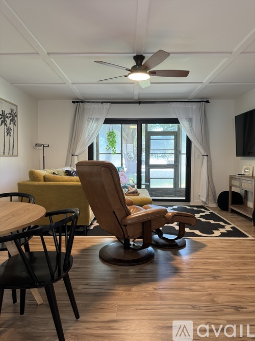A living room with a yellow sofa, a wooden chair, and a ceiling fan.