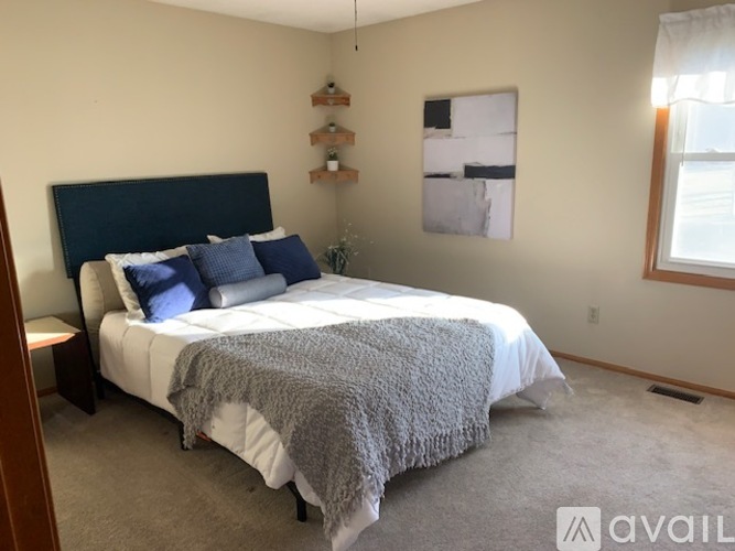 A bedroom with a bed covered in a grey blanket and blue pillows.