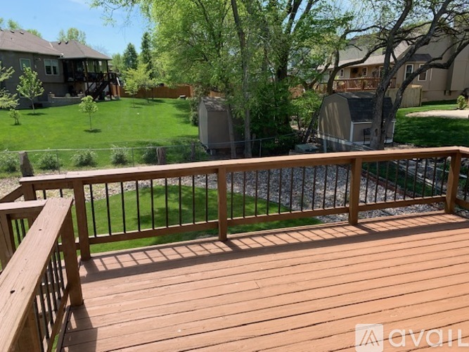 A deck with a railing overlooking a backyard with a lawn and trees.