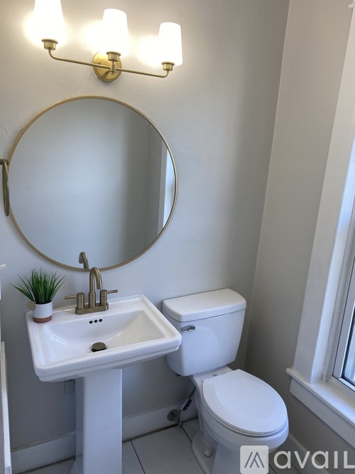 A bathroom with a toilet, sink, mirror, and light fixture.