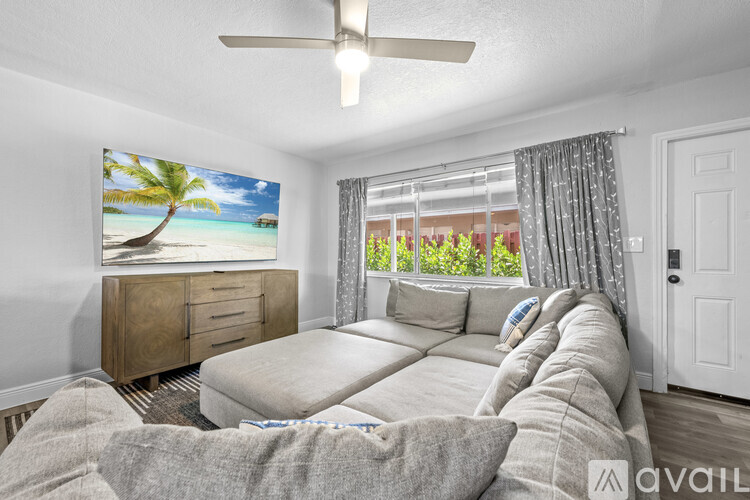 A living room with a large couch, a dining table with chairs, and a painting of a beach scene on the wall.