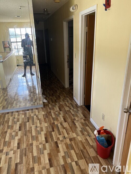 A man in a bathroom with a wooden floor and a red bucket.
