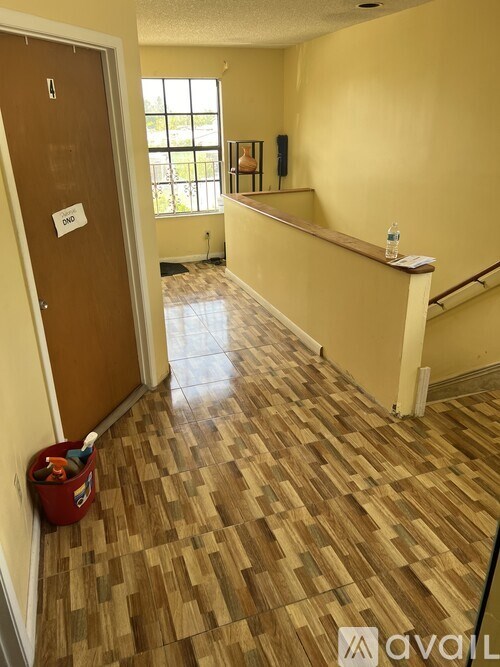 A hallway with a wooden floor and a red bucket on the floor.