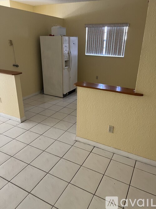 A kitchen area with a refrigerator, tiled floor, and a window with blinds.
