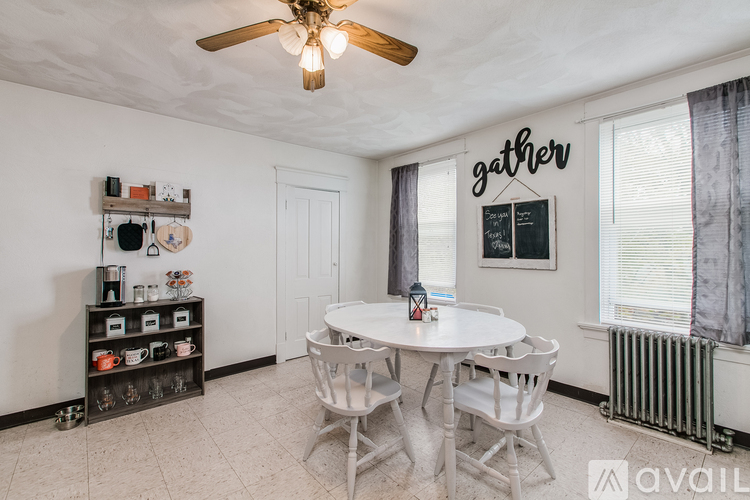 A dining room with a white table and chairs, a ceiling fan, and a shelf with various items.