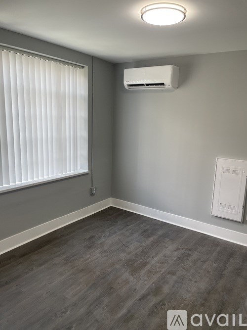 A room with a window covered by white blinds and a wall-mounted air conditioning unit.