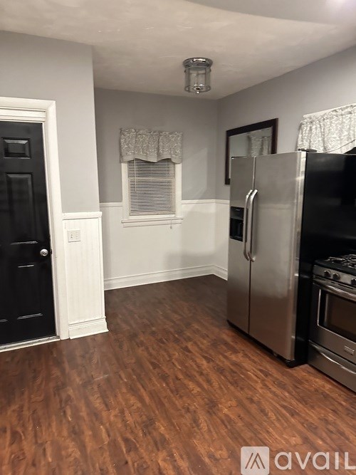A kitchen with a black door, a stainless steel refrigerator, and a wooden floor.