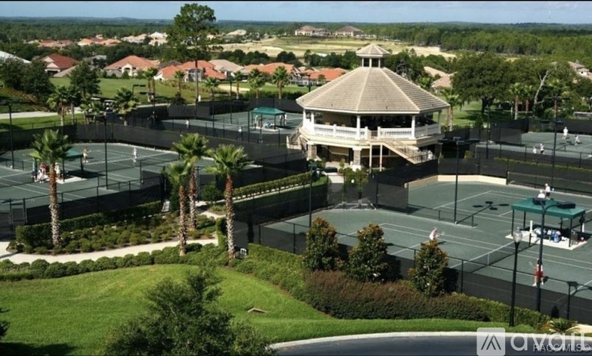 A tennis court surrounded by a green fence and a gazebo in the background.