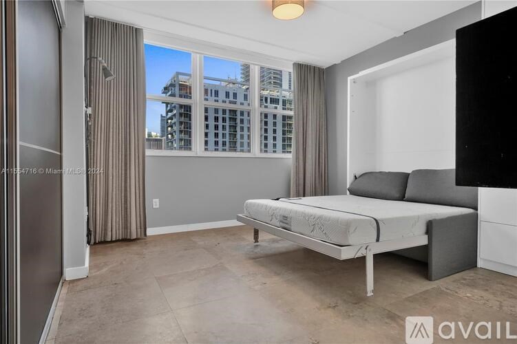 A bedroom with a large bed and a view of a building outside the window.