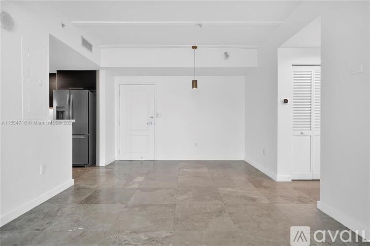A spacious, empty room with a kitchen area in the background.